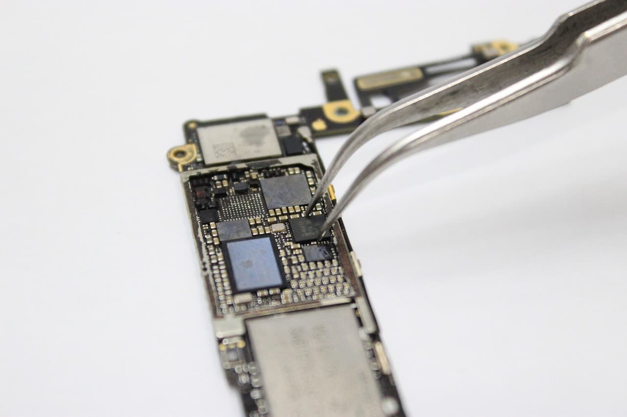 Pince de précision posée sur la carte mère d'un smartphone, au-dessus du processeur et des puces mémoire